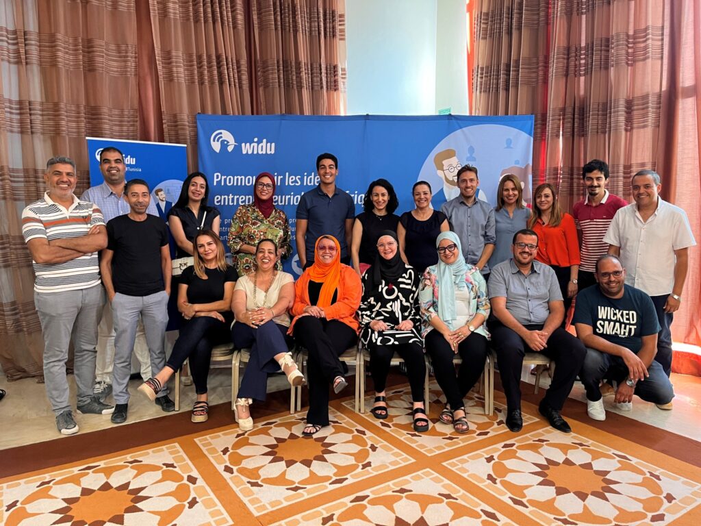 A diverse group of individuals smiling and posing together in front of a colorful banner at an event